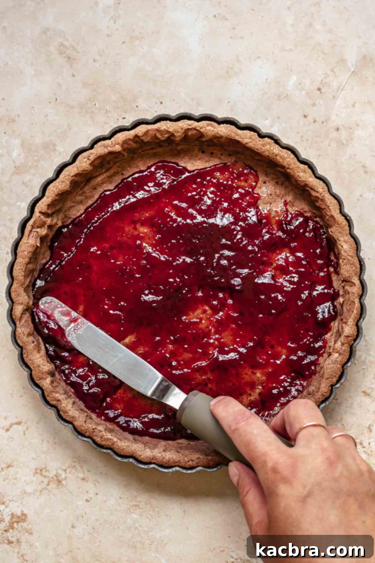 Decadent Chocolate Raspberry Delight 6 An offset spatula spreads raspberry jam onto a cooked tart crust.