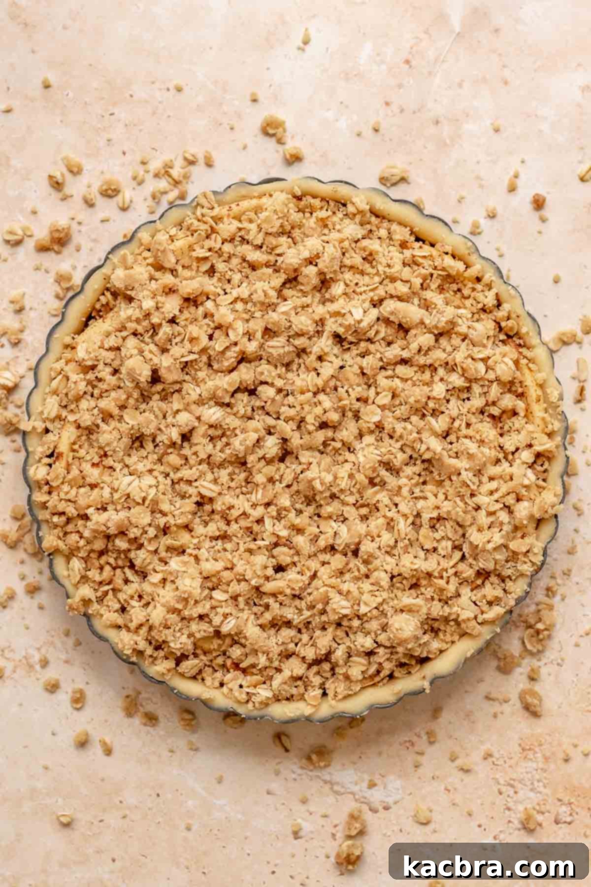 Cinnamon Apple Crumble Tart 12 The remaining crumble topping generously covers an entire layer of perfectly arranged apples in a tart pan, ready for baking.