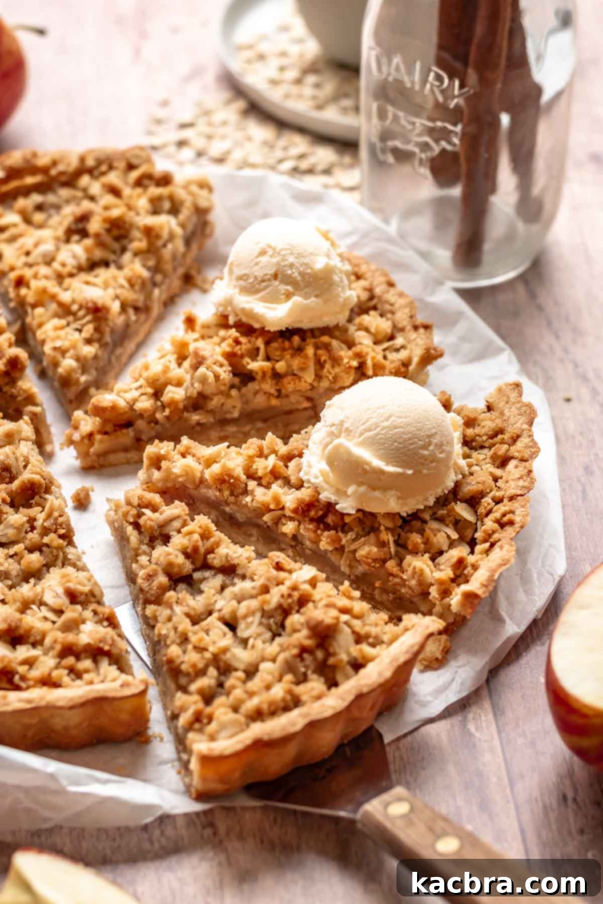 Cinnamon Apple Crumble Tart 14 A large, perfectly baked apple crumble tart, with several slices already removed, sitting on a wooden board. Two of the remaining slices are topped with ice cream, ready to be served.