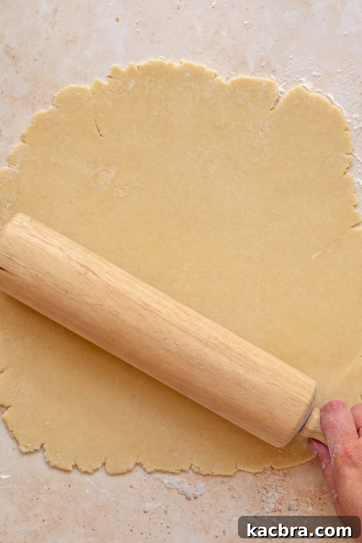 Cinnamon Apple Crumble Tart 4 A wooden rolling pin carefully rolls out sweet tart dough on a lightly floured surface, demonstrating the initial step of crust preparation.