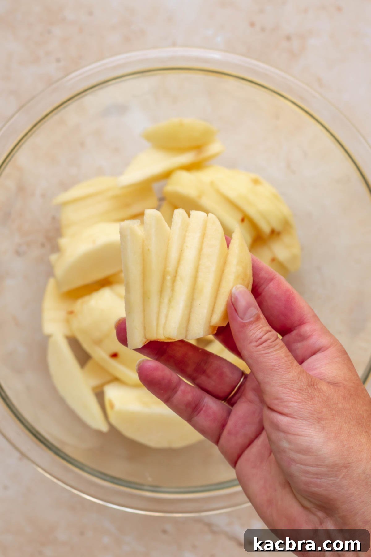 Cinnamon Apple Crumble Tart 9 A hand holds a fanned arrangement of thinly sliced apples, ready to be placed into the tart crust.