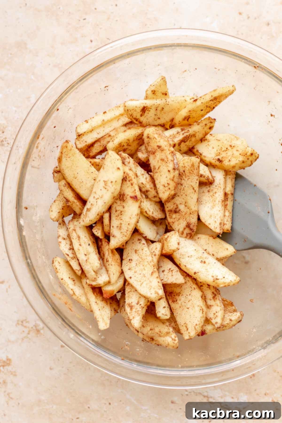 Cinnamon Apple Crumble Tart 10 A spatula gently mixes apple slices with flour and spices in a large mixing bowl, ensuring each slice is thoroughly coated.