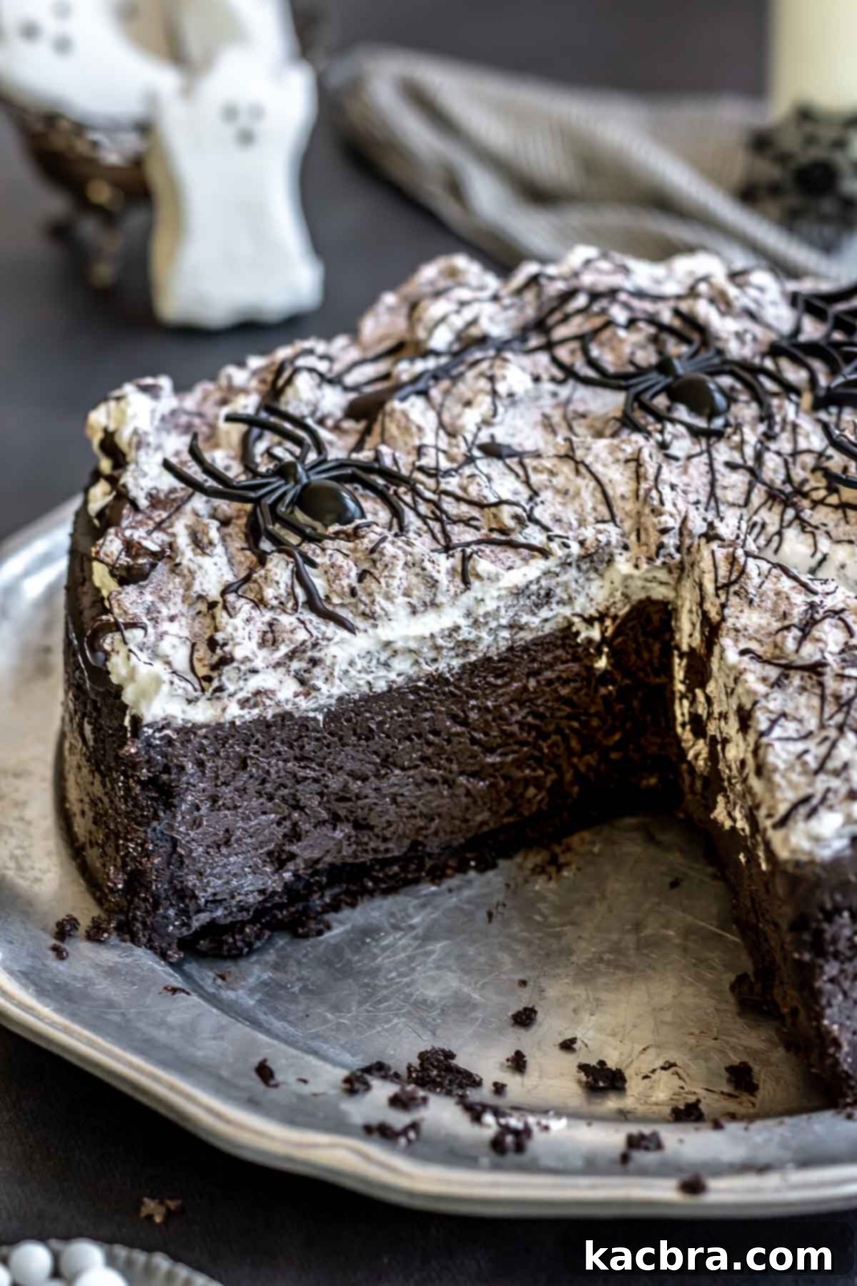 A Halloween cheesecake decorated with plastic spiders and Oreo crumbs, ready for serving.