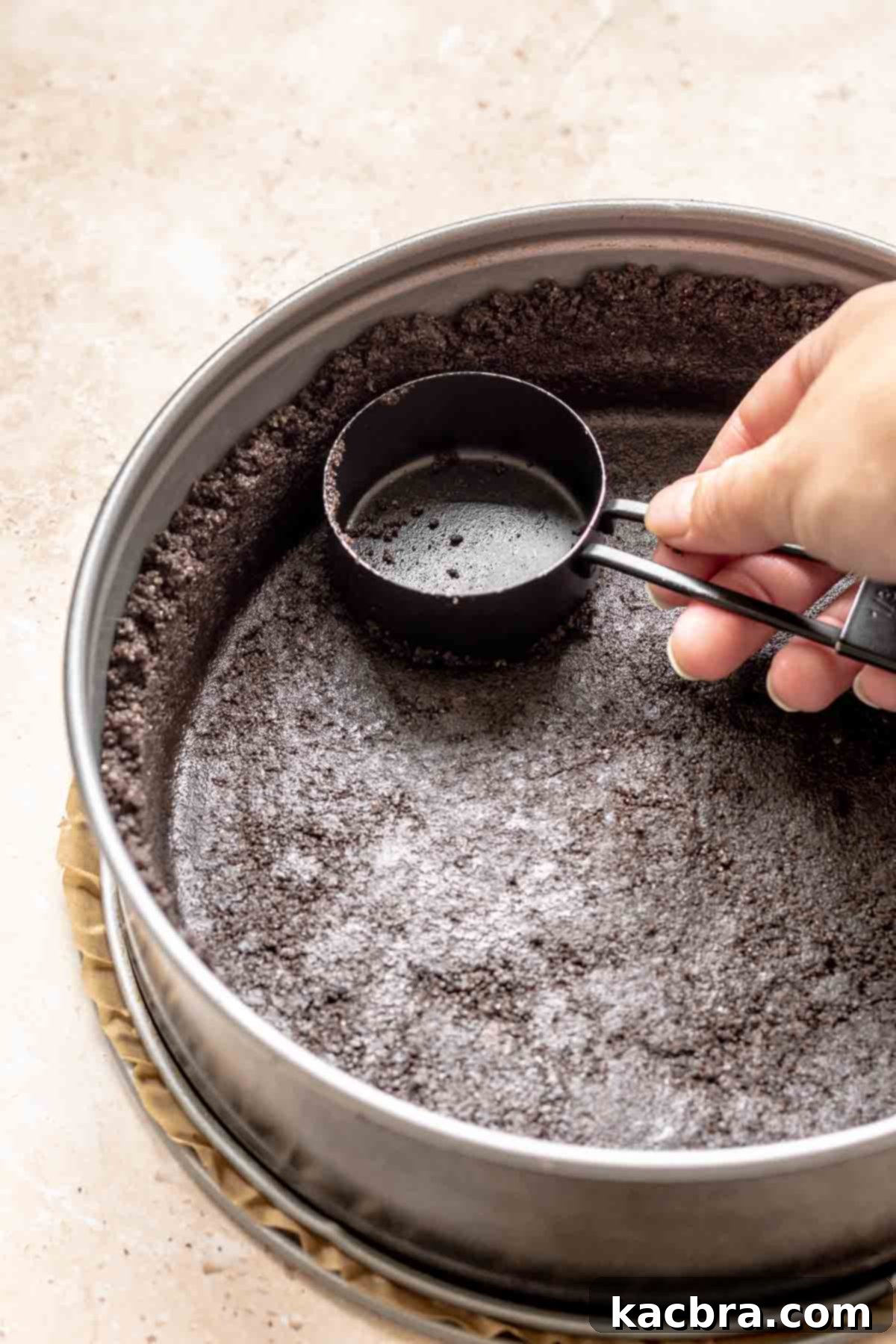 A hand presses oreo crumbs into a springform pan.