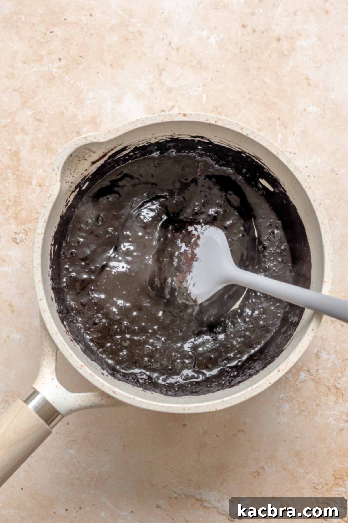 Black cocoa powder, water and cream blooming in a saucepan with a spatula.
