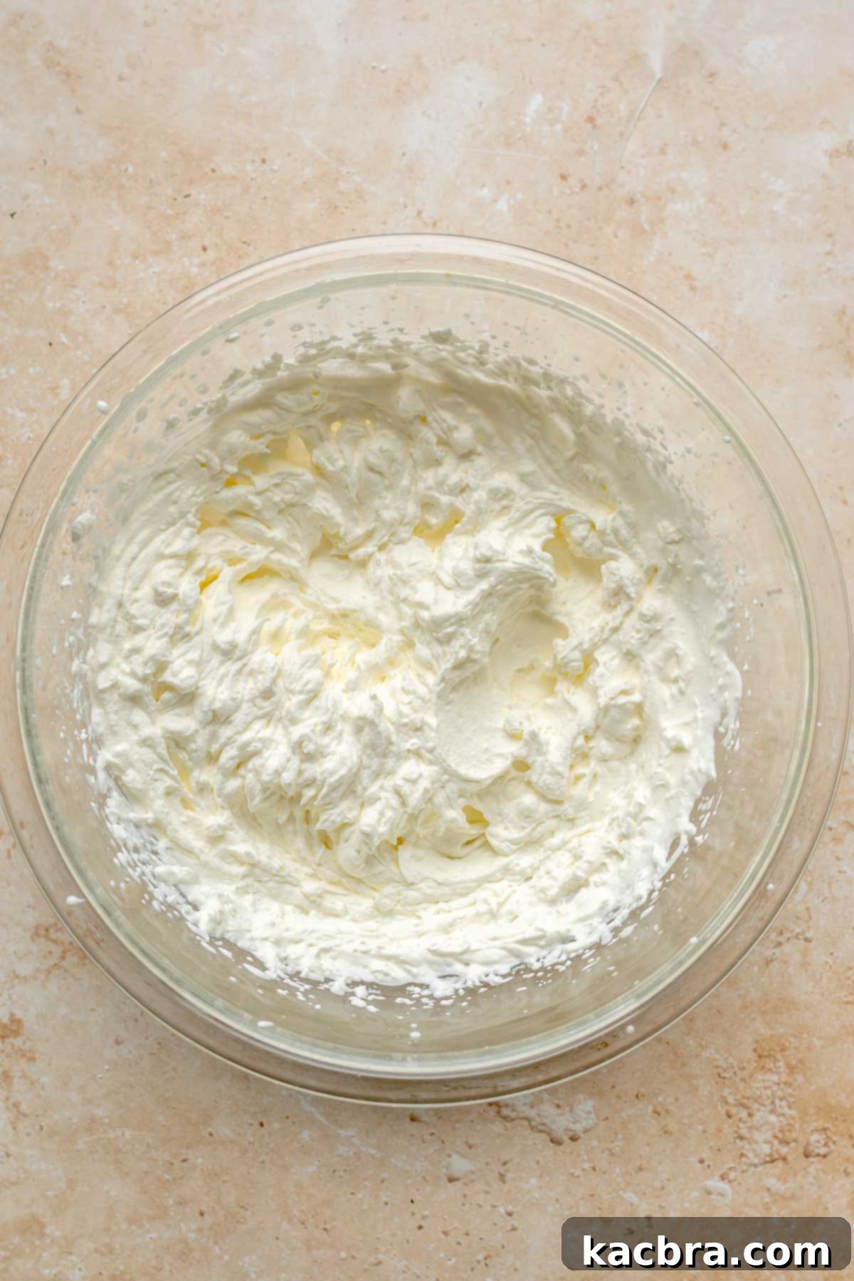 Stiff peaks of whipped cream in a mixing bowl, ready for folding into the cheesecake batter.