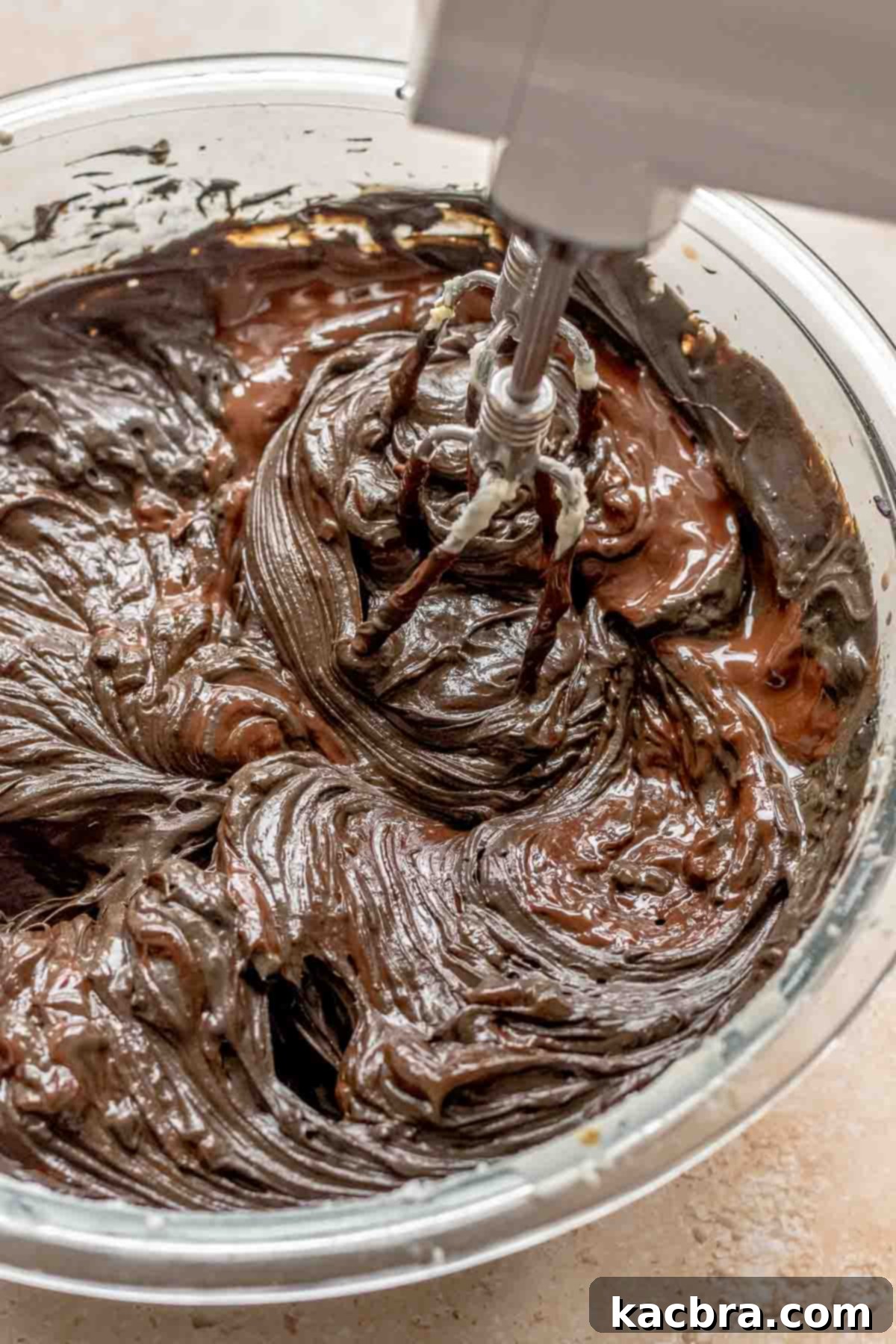 A hand mixer mixing melted chocolate in a mixing bowl.