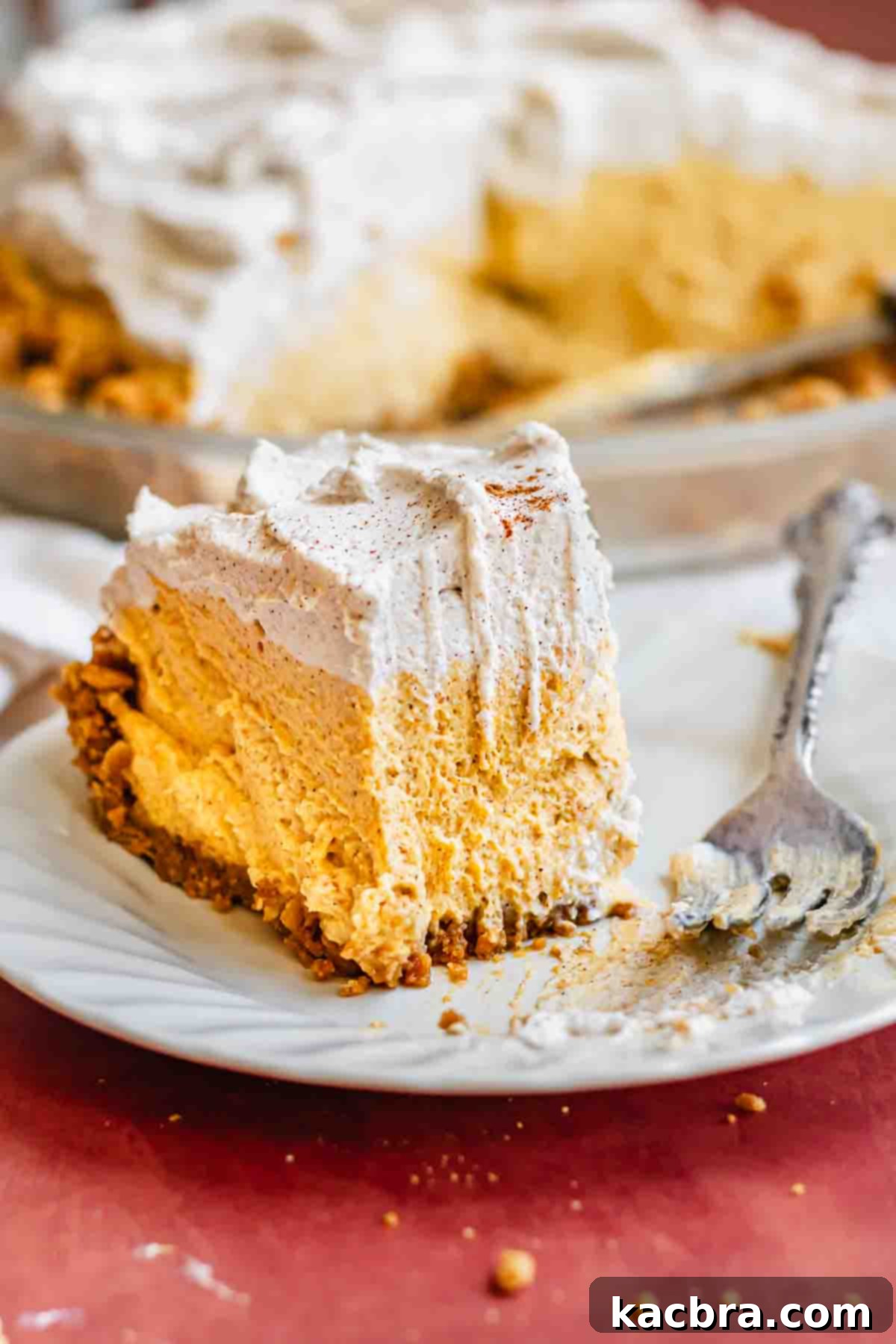 Creamy Pumpkin Cloud 2 A beautifully presented slice of pumpkin mousse pie on a white plate, showcasing its distinct layers of gingersnap crust, airy pumpkin mousse, and whipped cream topping.