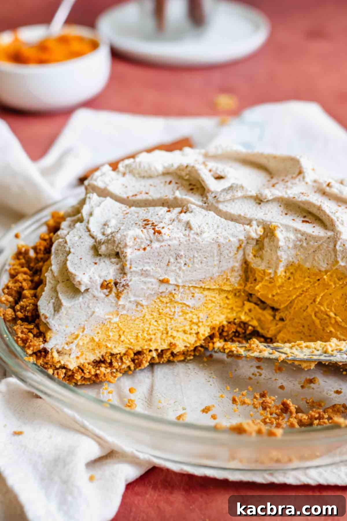 Creamy Pumpkin Cloud 11 A fully assembled pumpkin mousse pie, with a slice removed, revealing the layers of crust, mousse, and a fluffy cinnamon maple whipped cream topping.