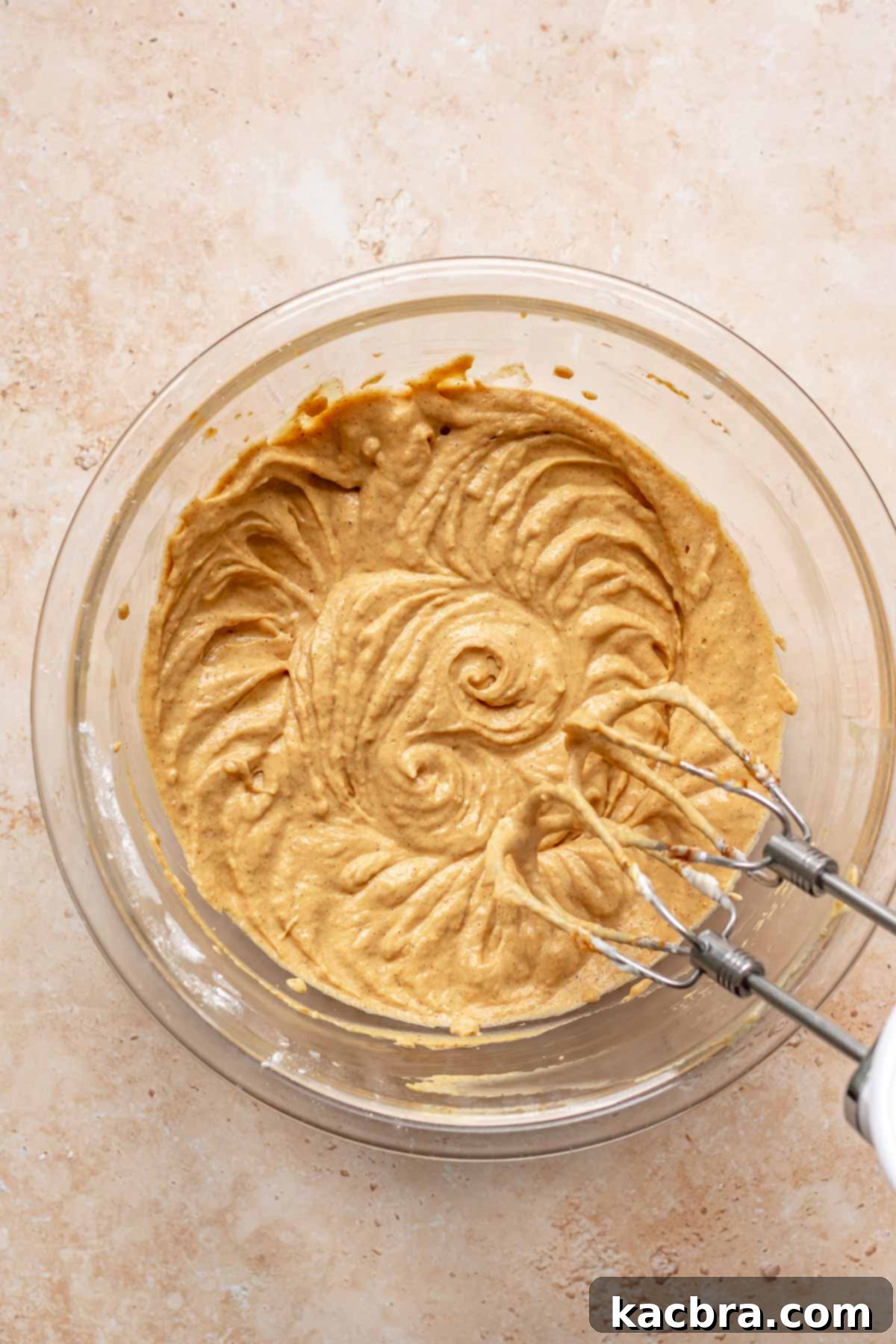 Creamy Pumpkin Cloud 7 Pumpkin puree, spices, and vanilla extract being mixed into the cream cheese batter in a bowl with an electric hand mixer.