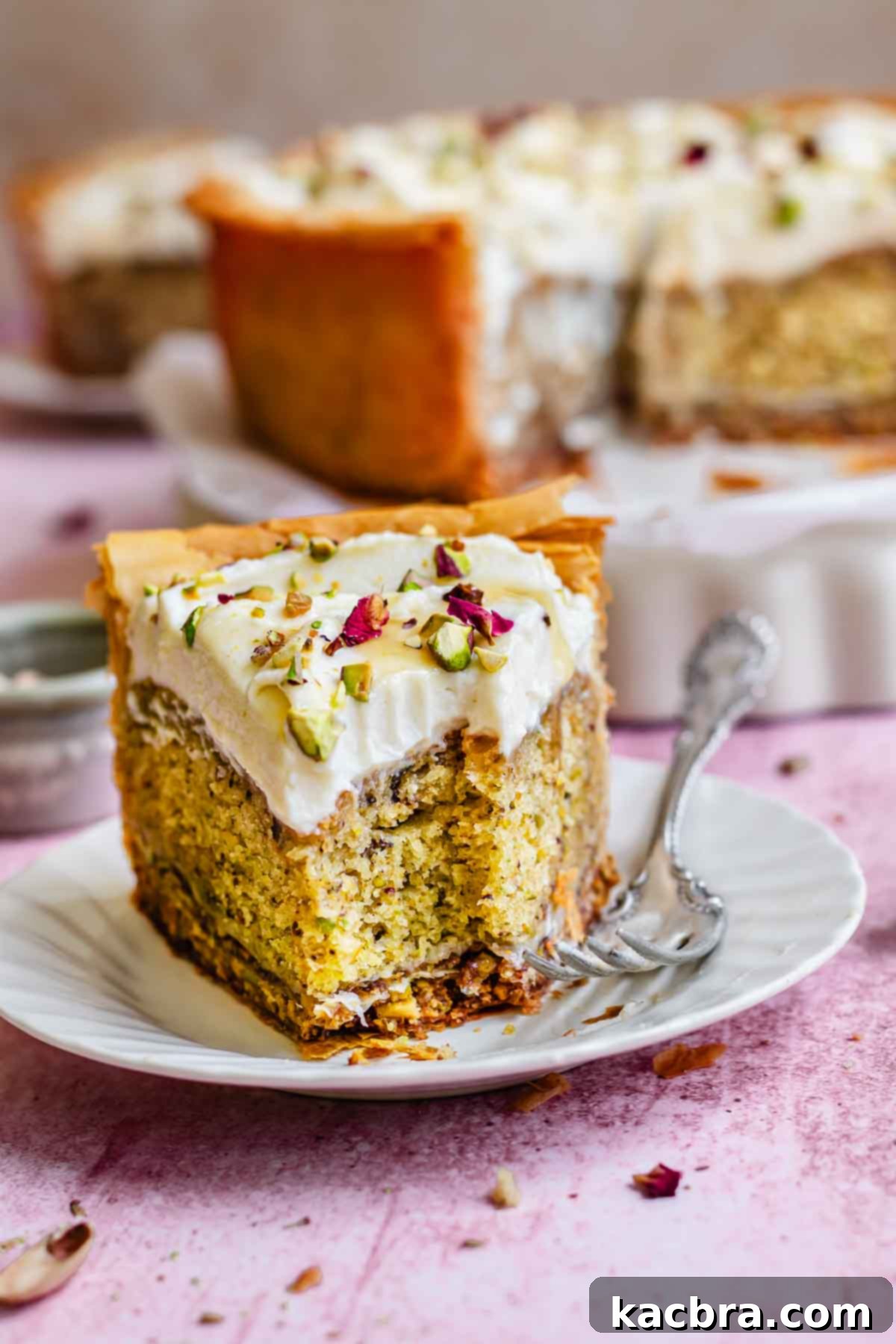 Golden Honey Baklava Dream Cake 21 A slice of pistachio cake with a bite removed on a white plate, showcasing moistness.