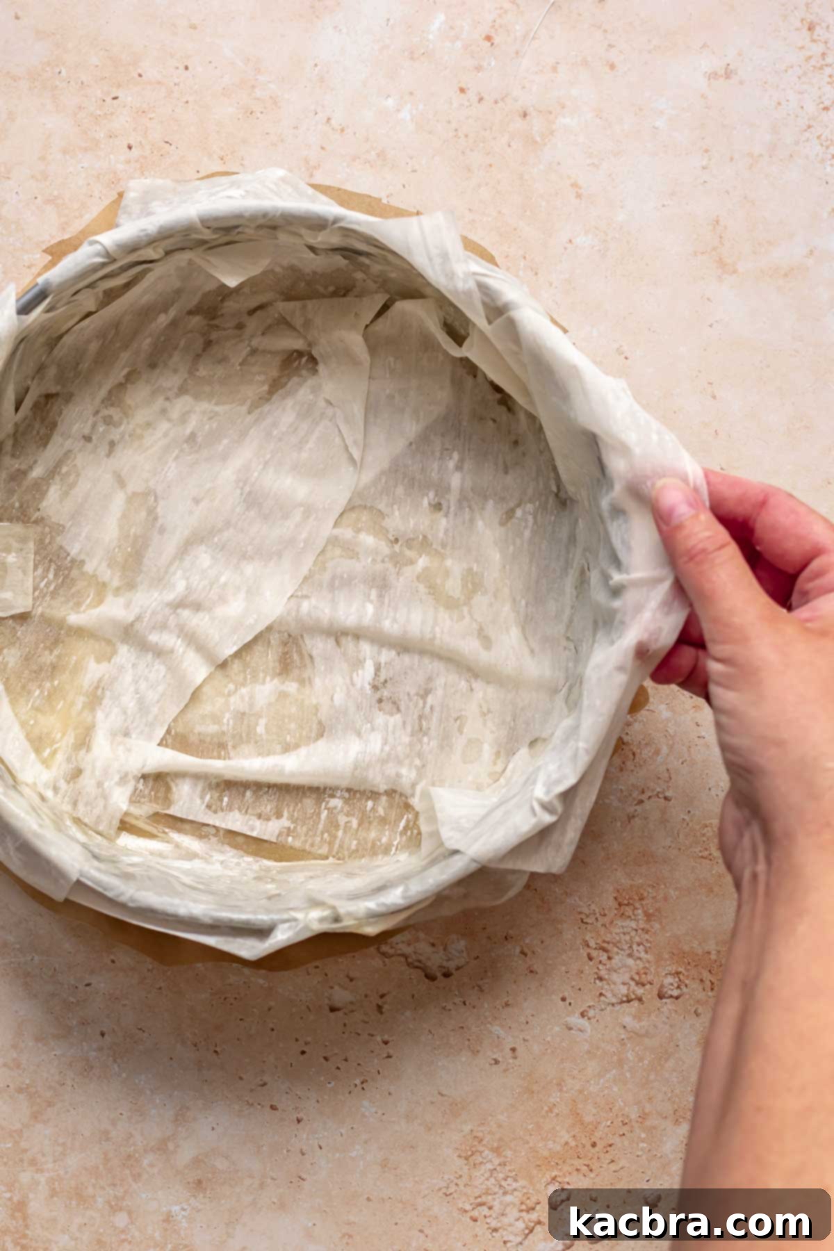 Golden Honey Baklava Dream Cake 8 A hand places a fresh sheet of phyllo dough over the nut layers in a pan.