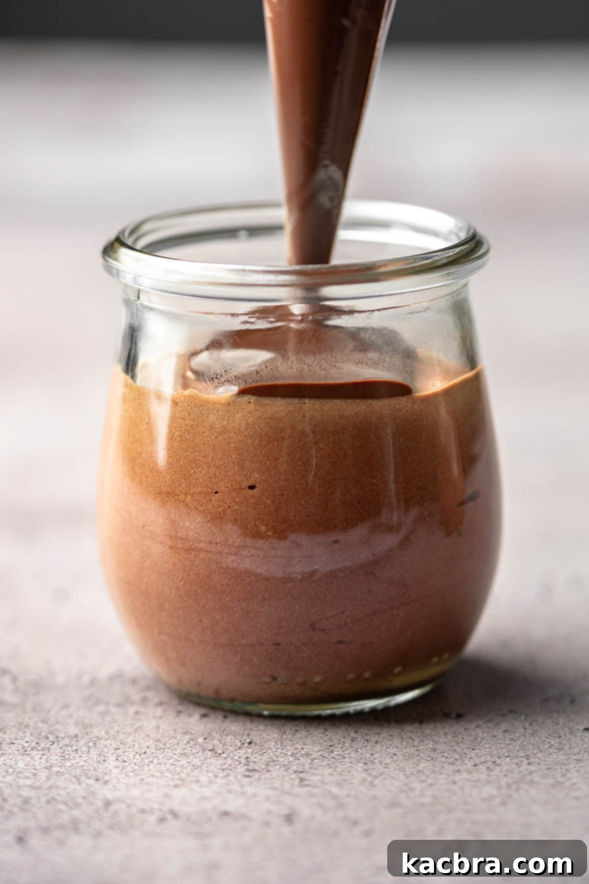 A piping bag adds chocolate ganache on top of the mousse in the cup.