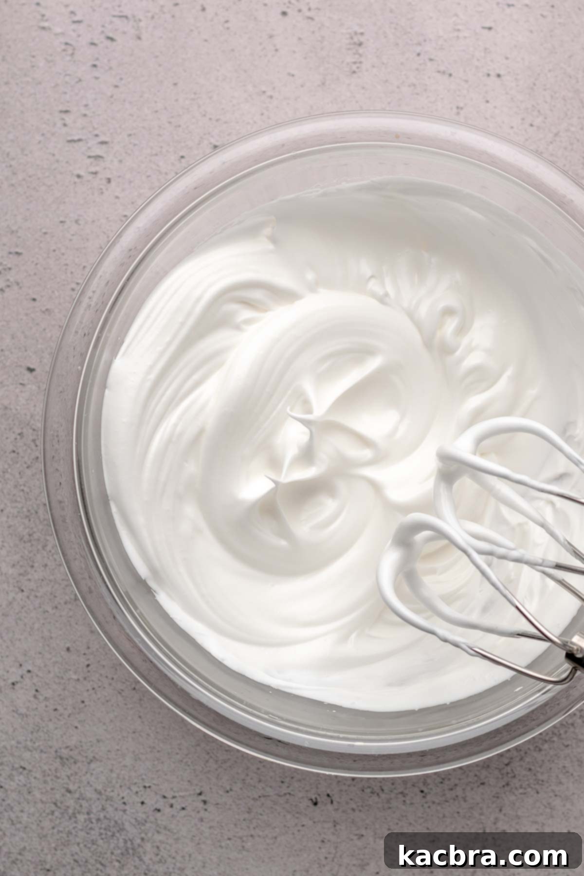 Beaters on the side of a bowl of whipped egg whites.