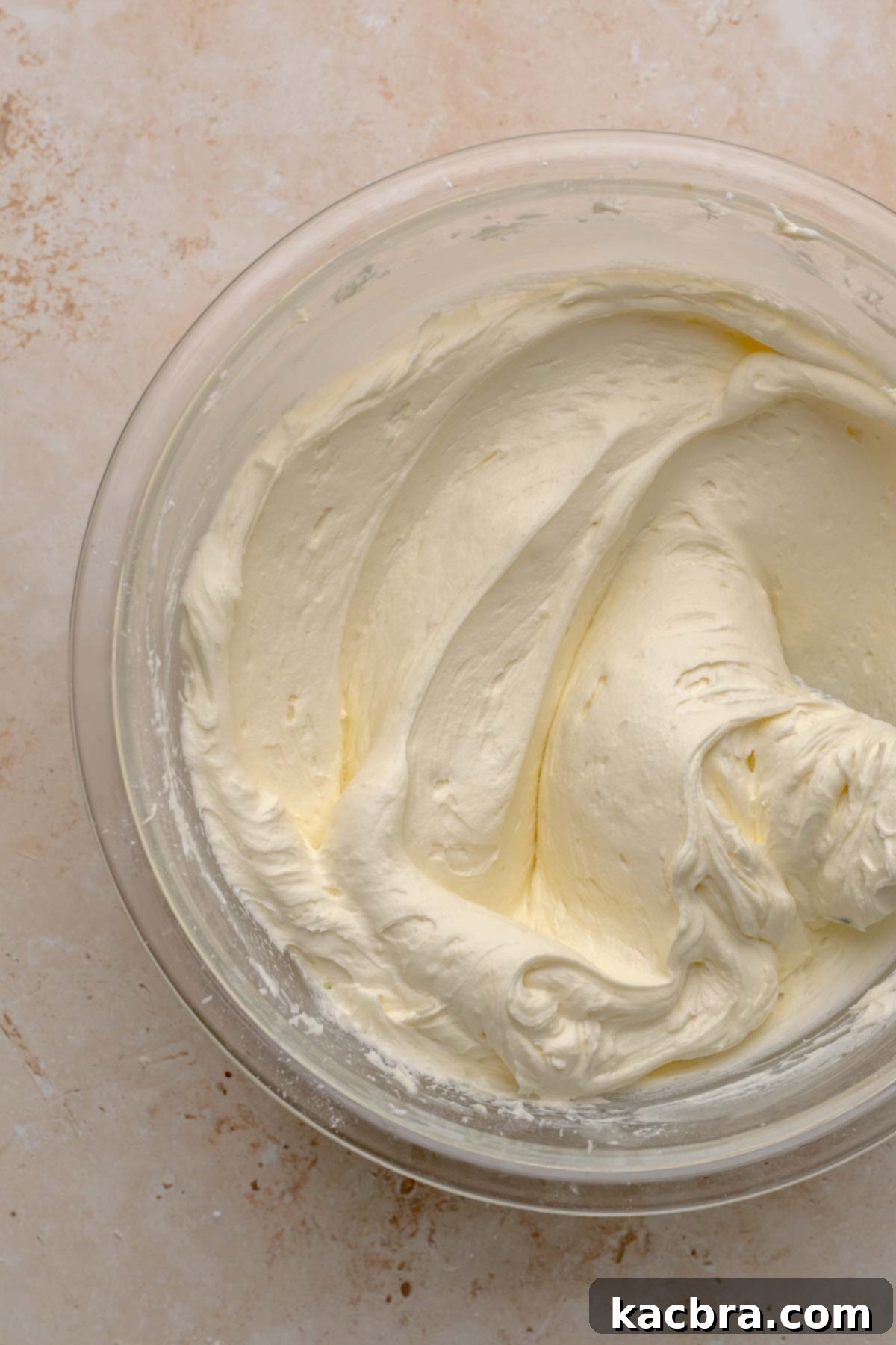 Fluffy white chocolate frosting in a mixing bowl, showing a perfect, pipeable consistency after adding heavy cream.