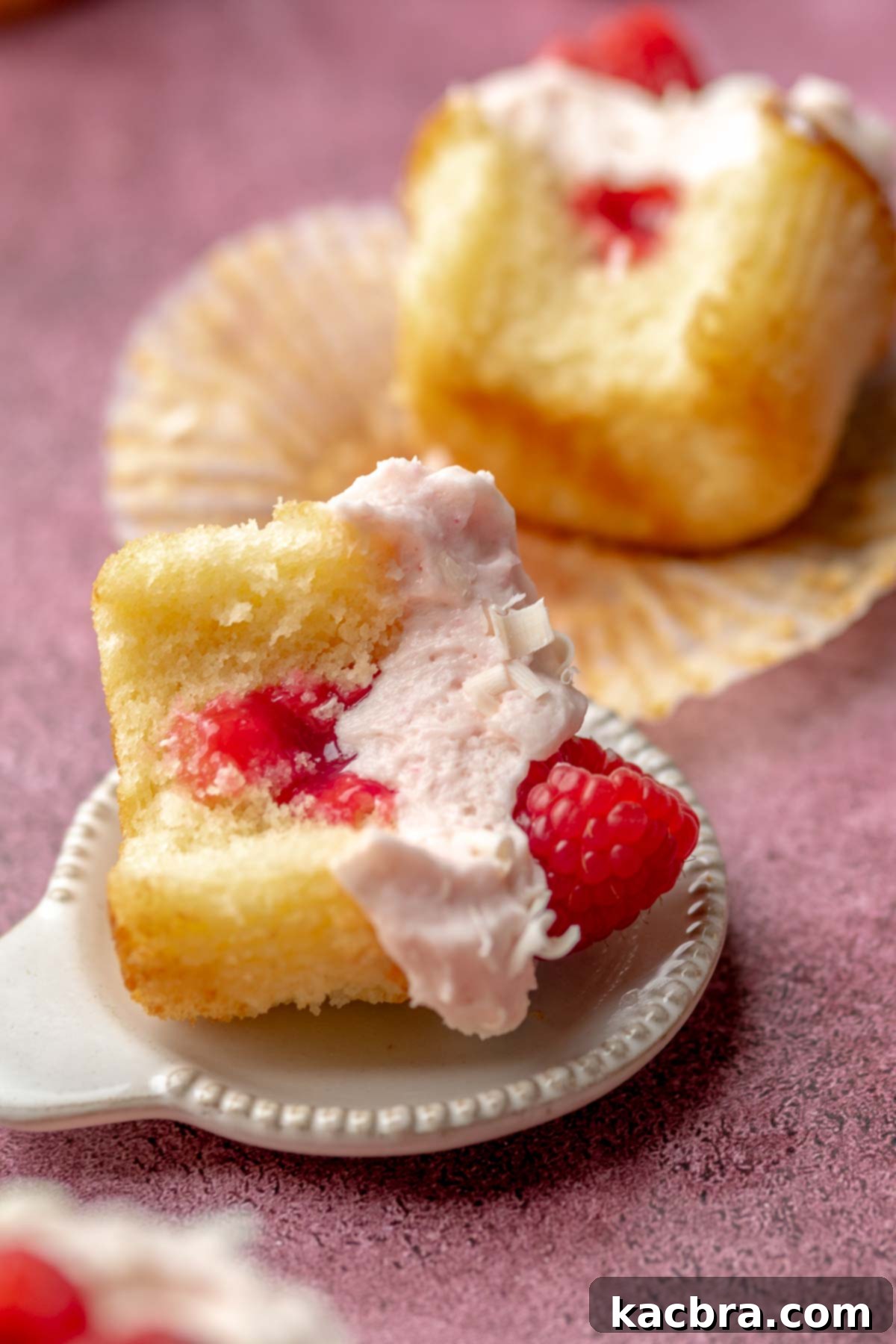 Ruby and Ivory Cupcake Delights 18 A raspberry white chocolate cupcake, with a bite taken out, lies on its side on a rustic wooden surface, showcasing its moist interior.