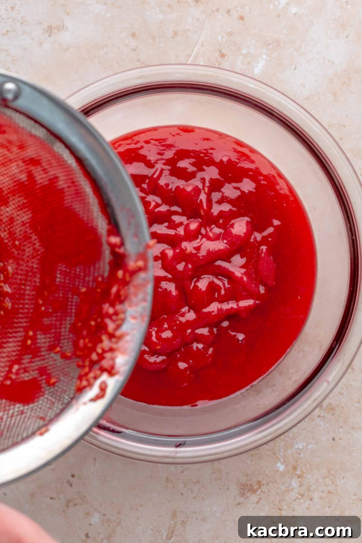 Ruby and Ivory Cupcake Delights 6 Thickened raspberry puree being pressed through a fine mesh sieve into a clean bowl, separating seeds from the smooth sauce.