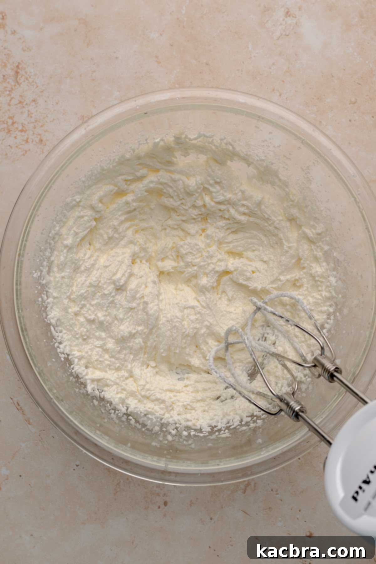 A hand mixer beats together butter, sugar, and oil in a large mixing bowl, creating a light and fluffy cupcake batter base.