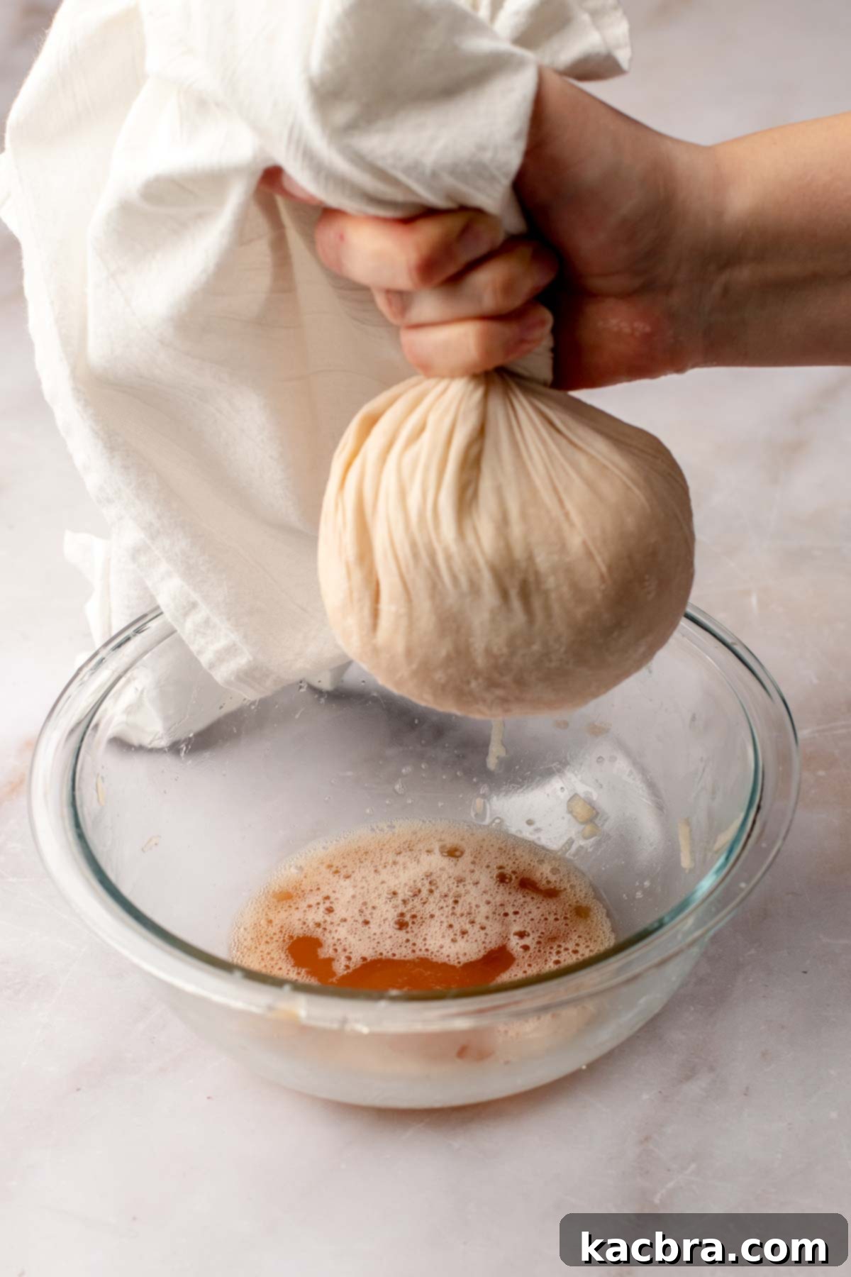 A hand wrings out potato water into a bowl.
