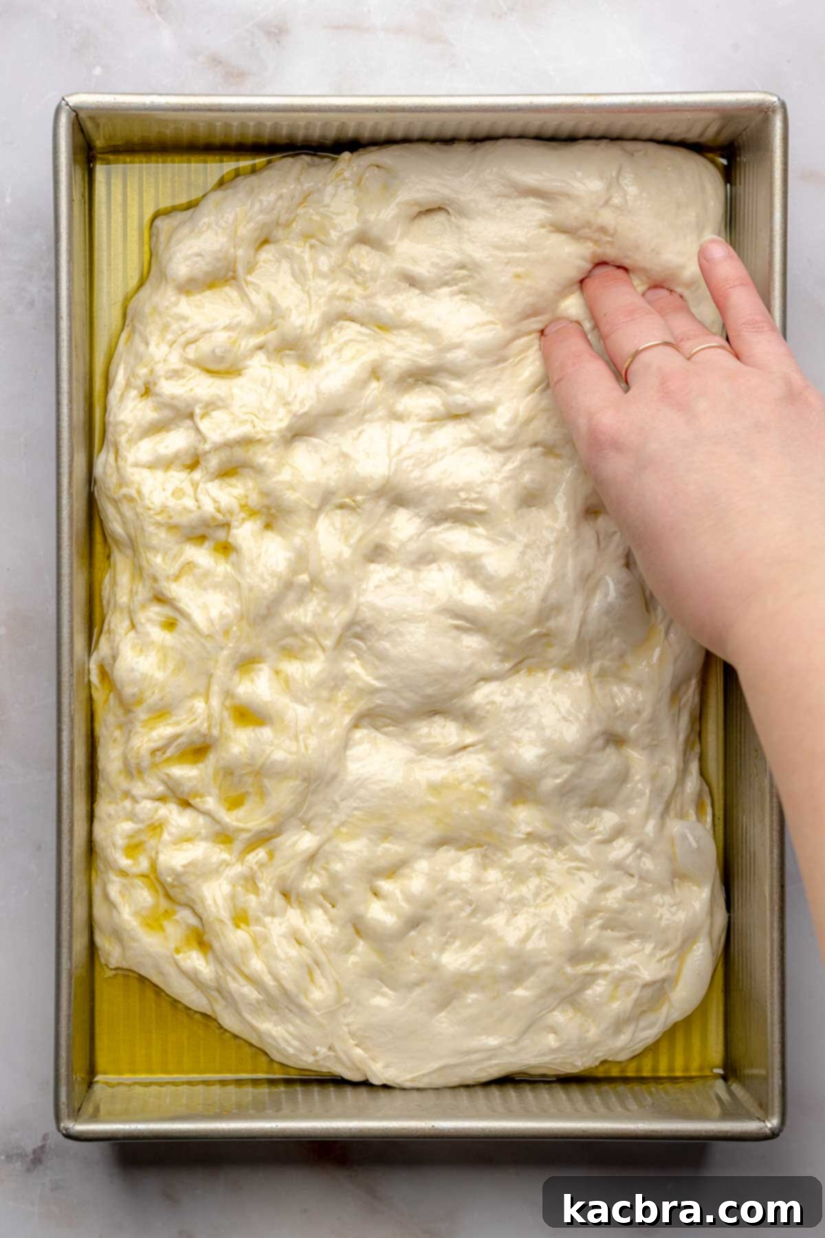 Aromatic Pesto Focaccia 12 A hand presses focaccia dough into the corners of the pan.