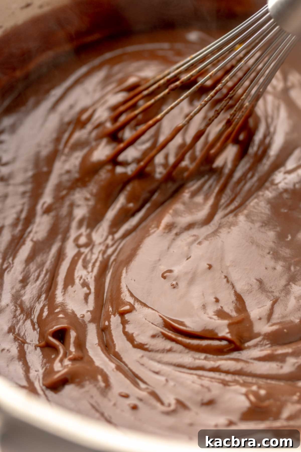Thick, bubbling chocolate pudding being vigorously whisked in a pot.