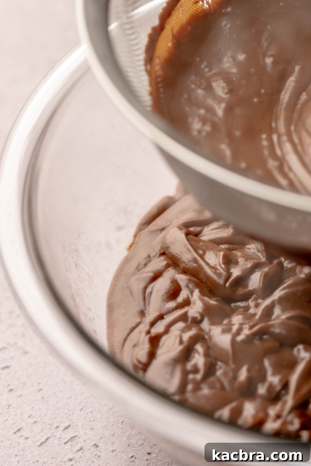 Smooth chocolate pudding being strained through a fine mesh sieve into a clean bowl.
