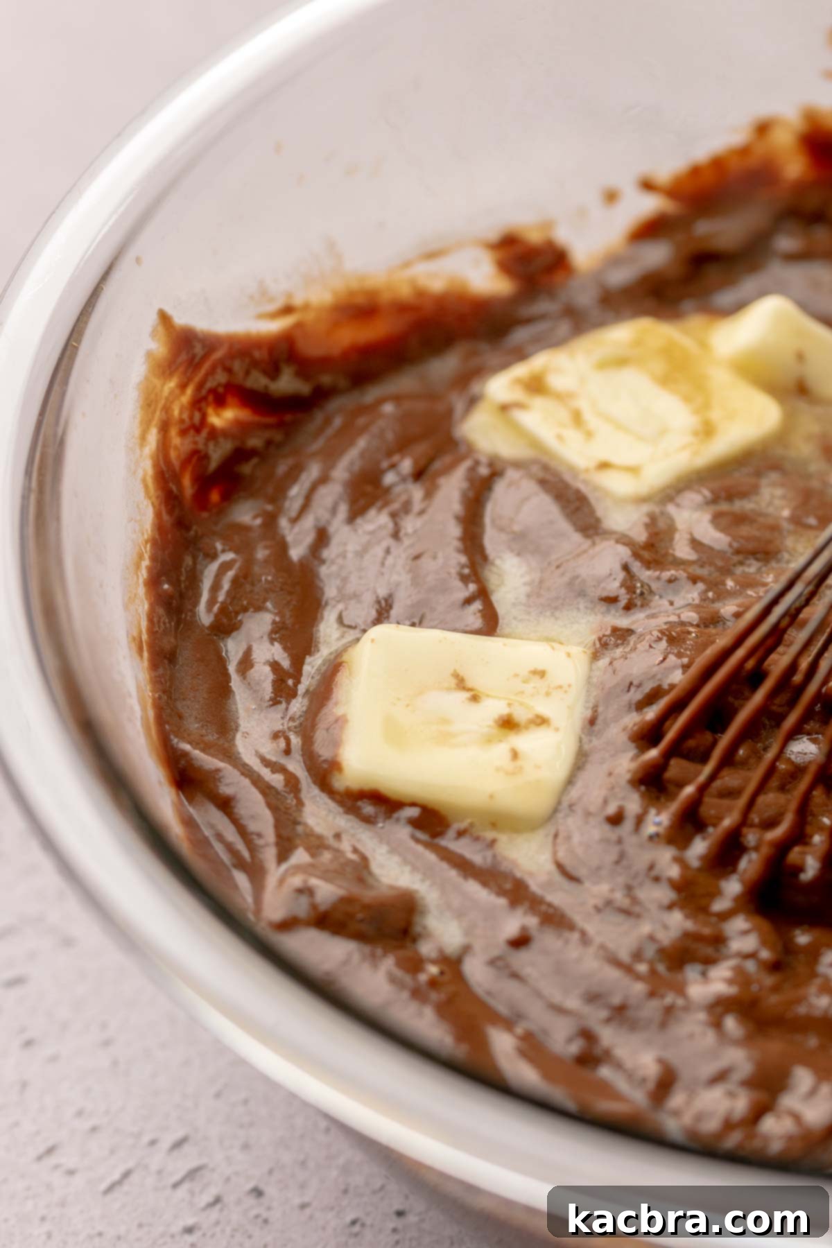 A whisk mixes butter into hot chocolate pudding in a bowl.