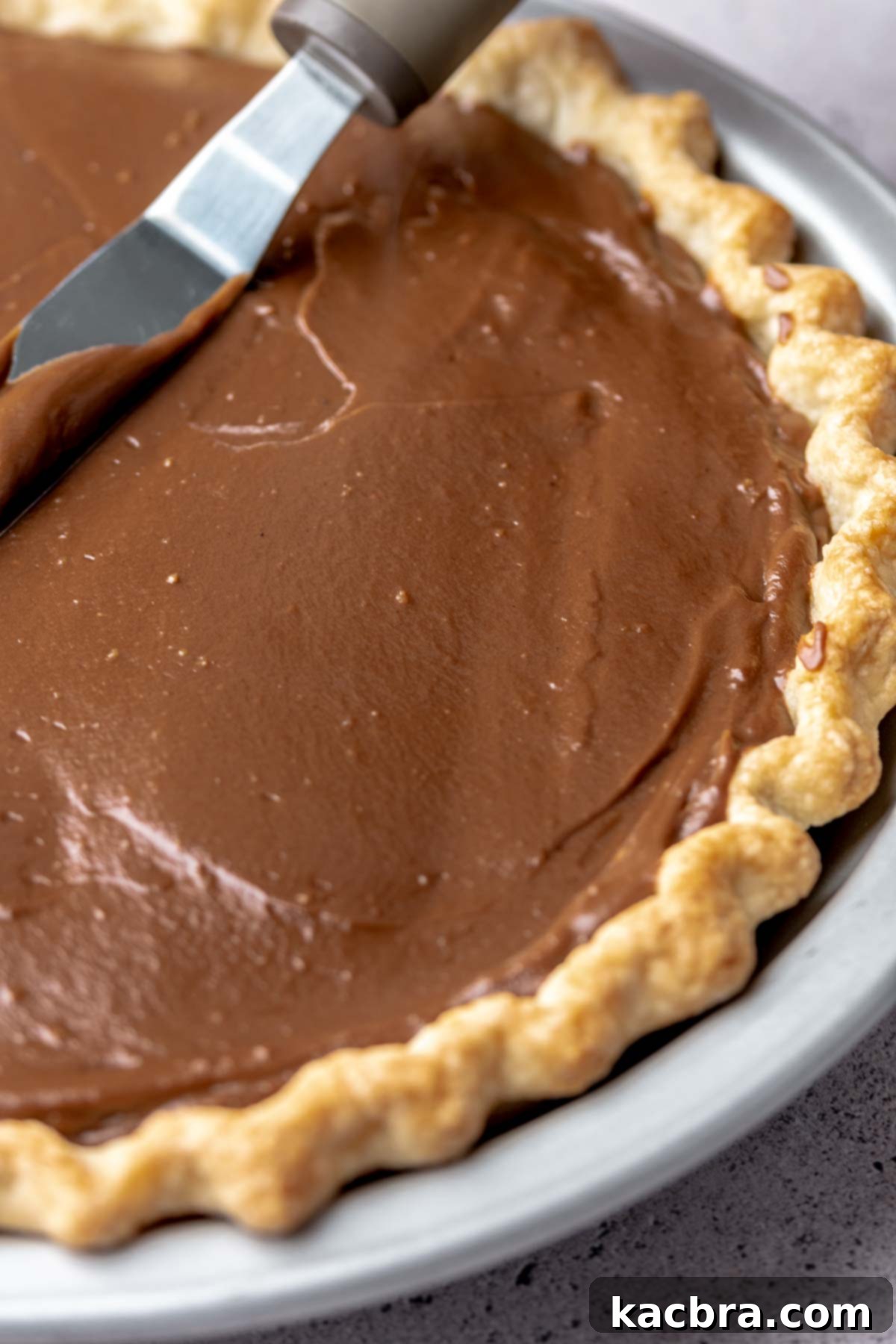 A spatula smoothing the chocolate pudding evenly into a blind-baked pie crust.