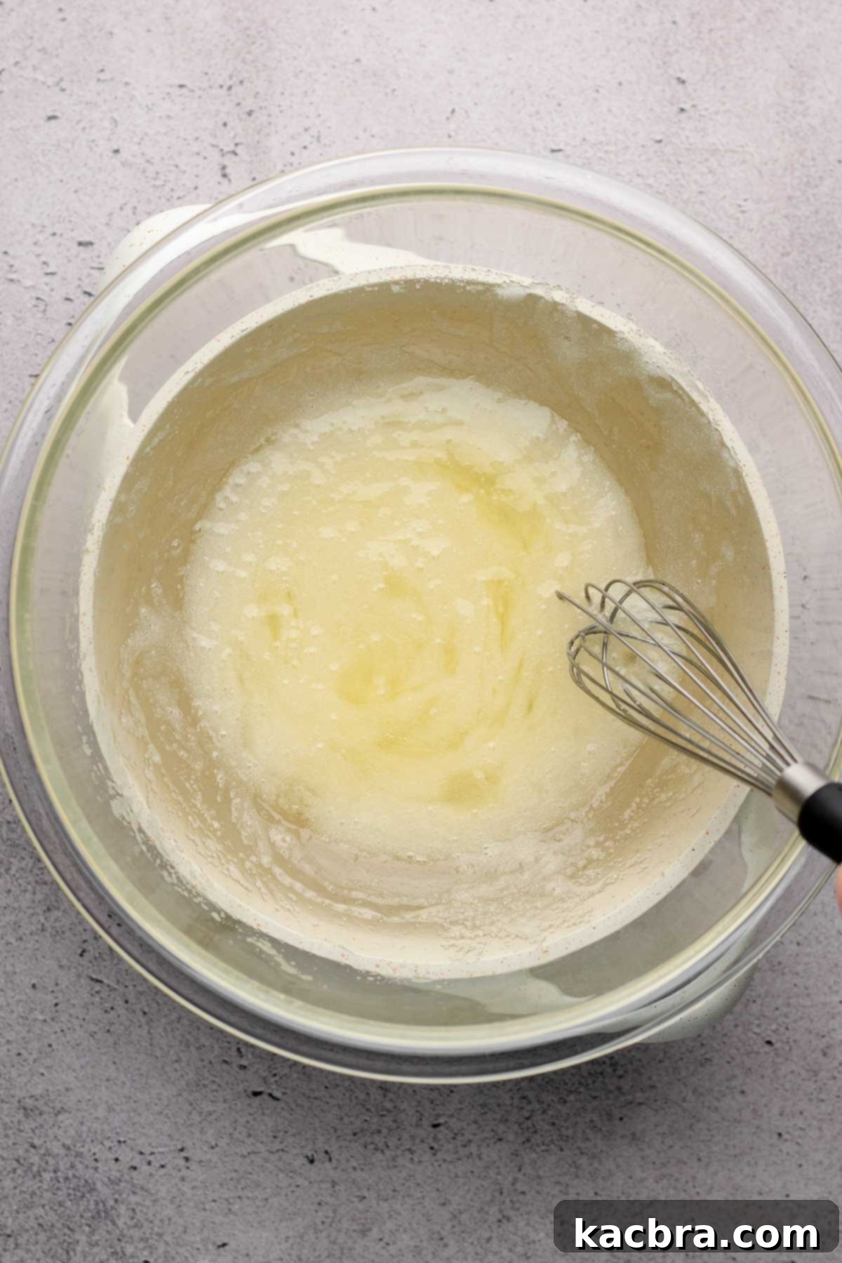 A whisk mixes sugar and egg whites together in a bowl on a Bain Marie.