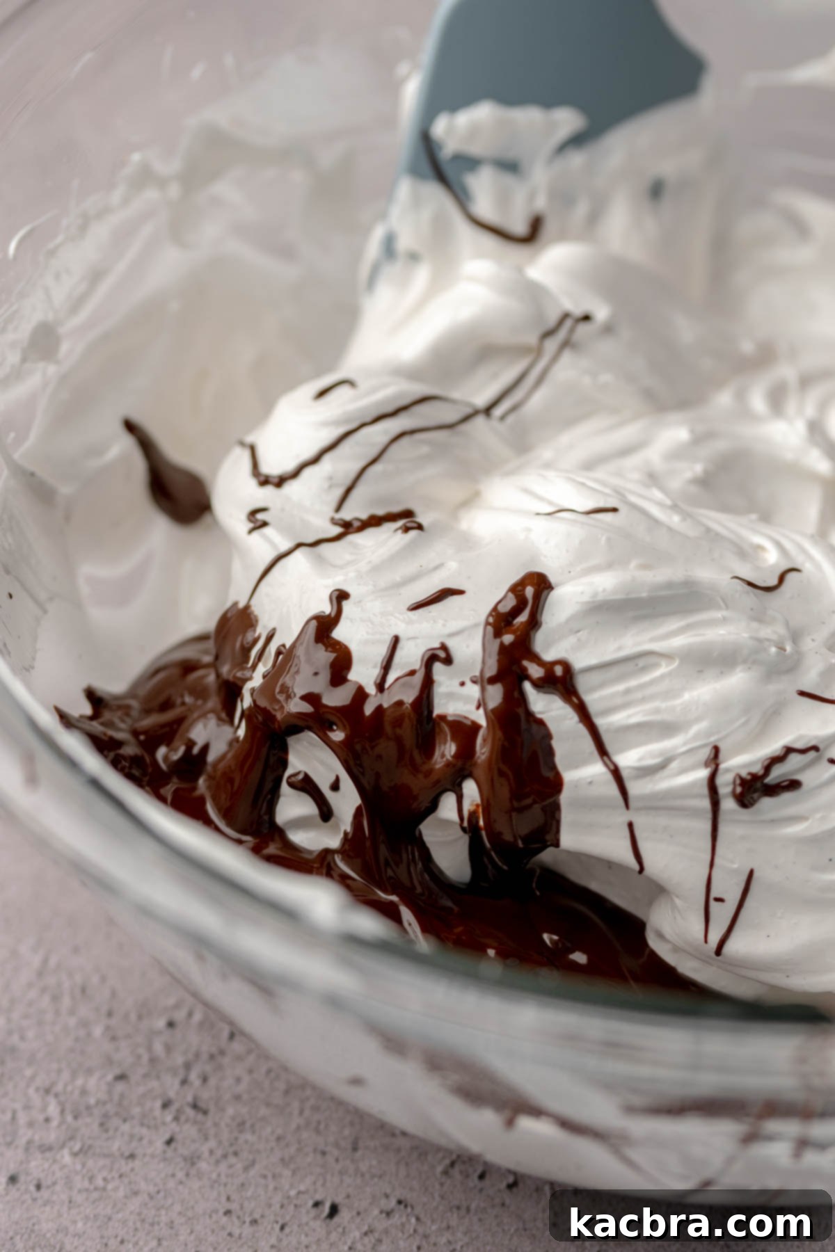 Melted chocolate drizzled onto one side of the whipped meringue in a bowl.