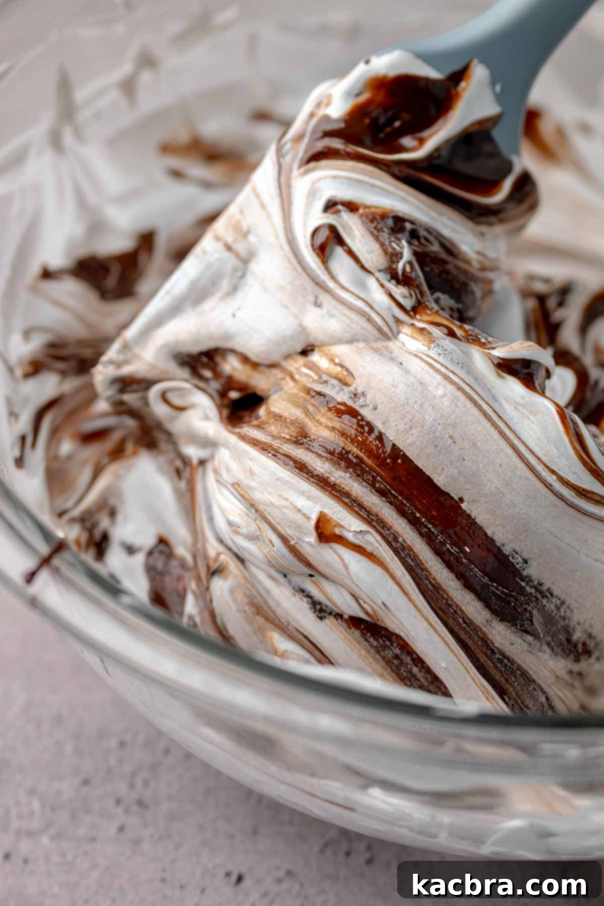 A spatula gently folding melted chocolate into meringue to create marbled streaks.