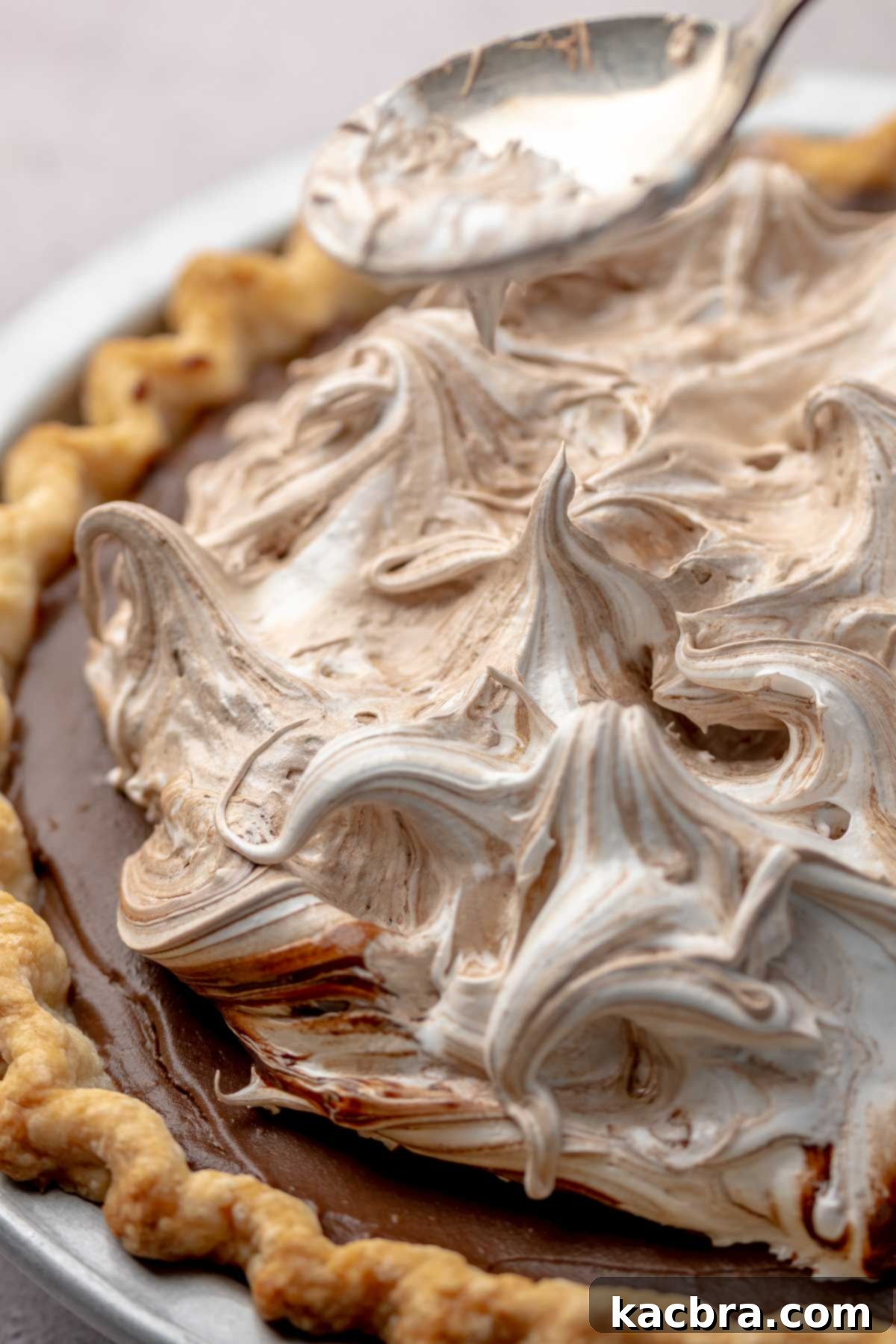 A spoon gently shaping peaks and swirls in the chocolate meringue on top of the pie.