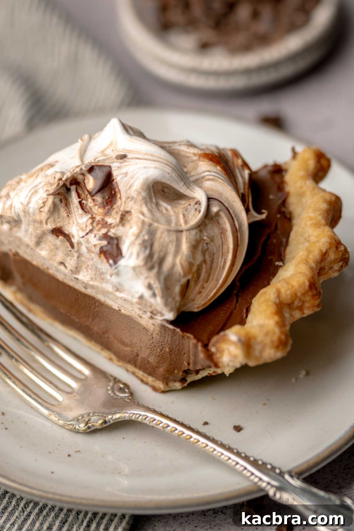 A slice of chocolate meringue pie on a plate with a fork next to it, inviting a taste.