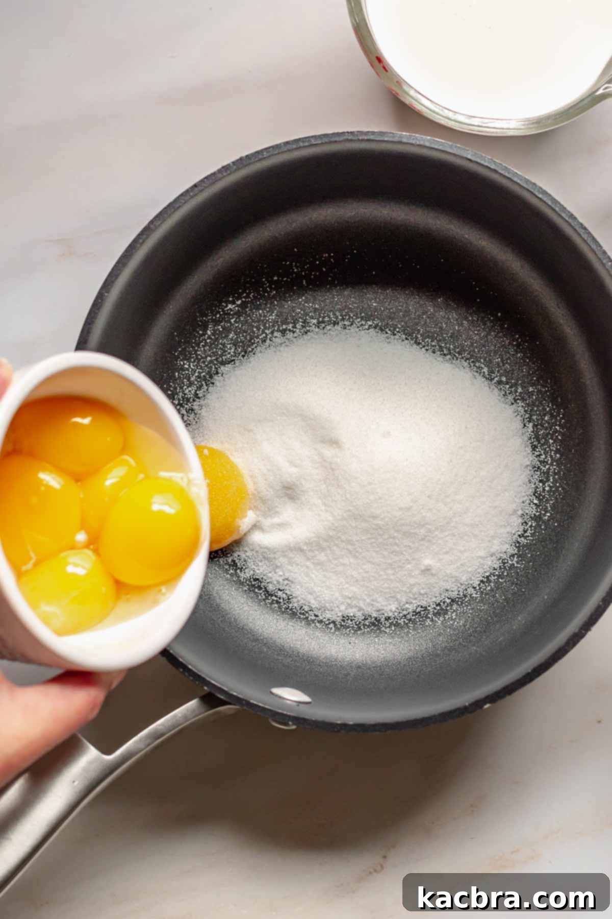 Egg yolks adding to sugar in a pot.