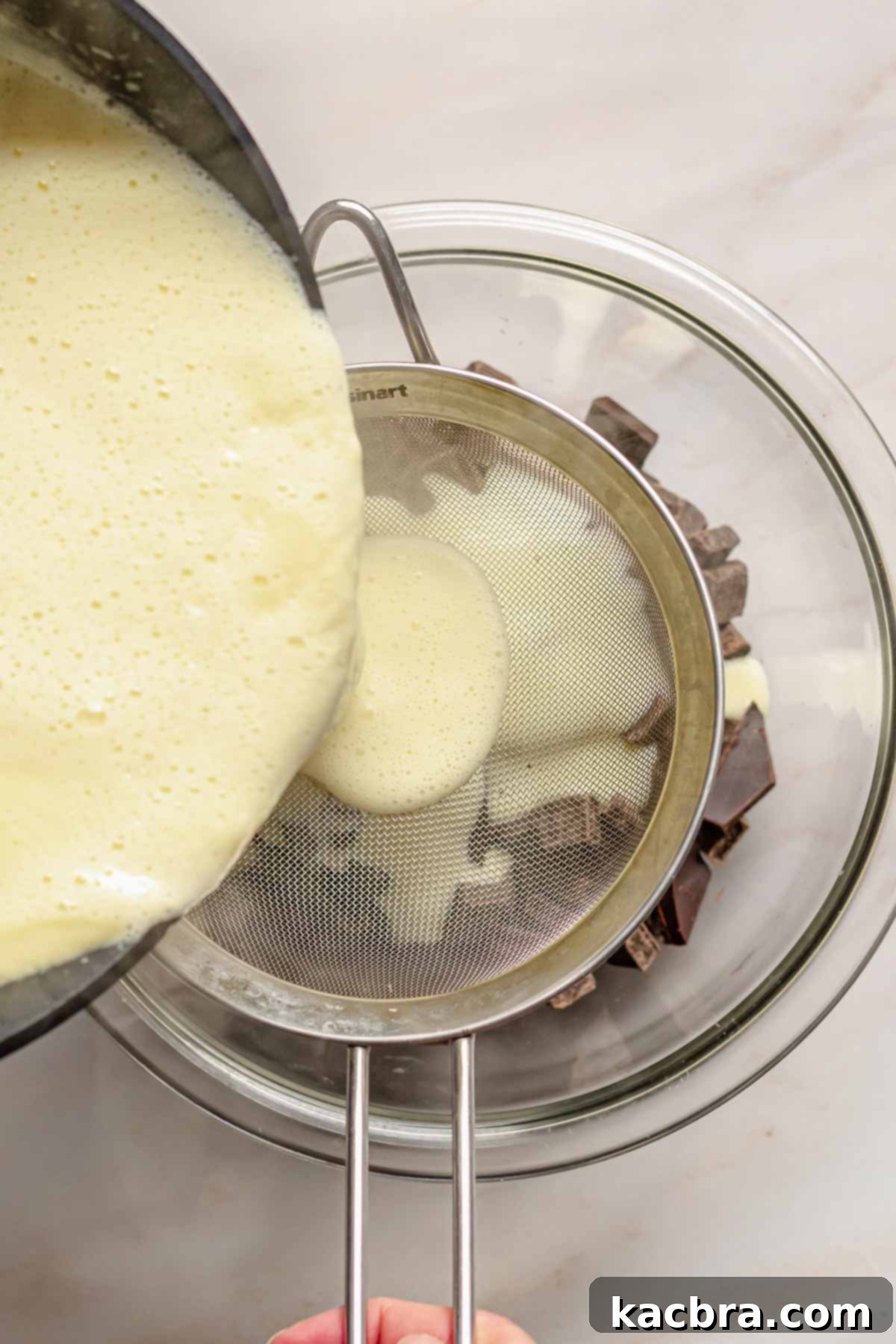 Custard cream pouring through a sieve into a bowl of chocolate.