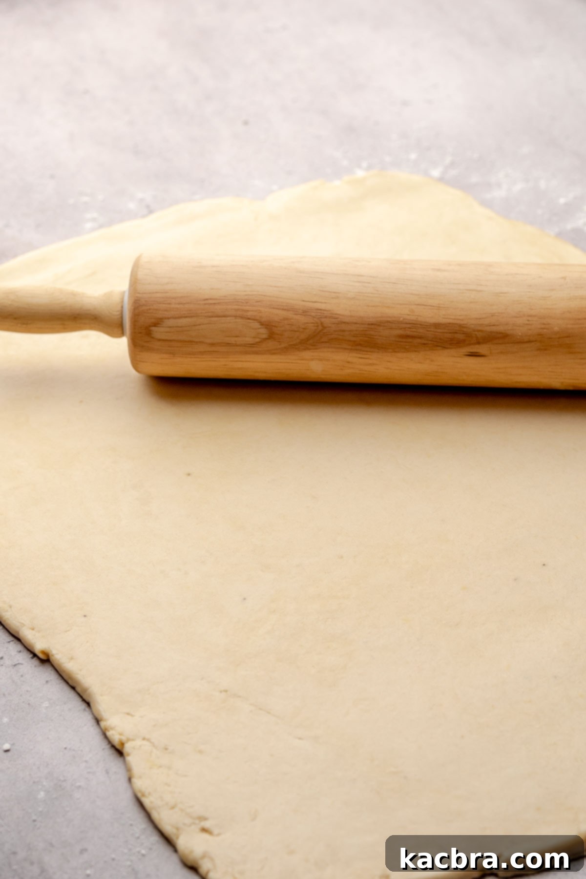 A rolling pin skillfully rolls out cinnamon roll dough into a large, even rectangle.
