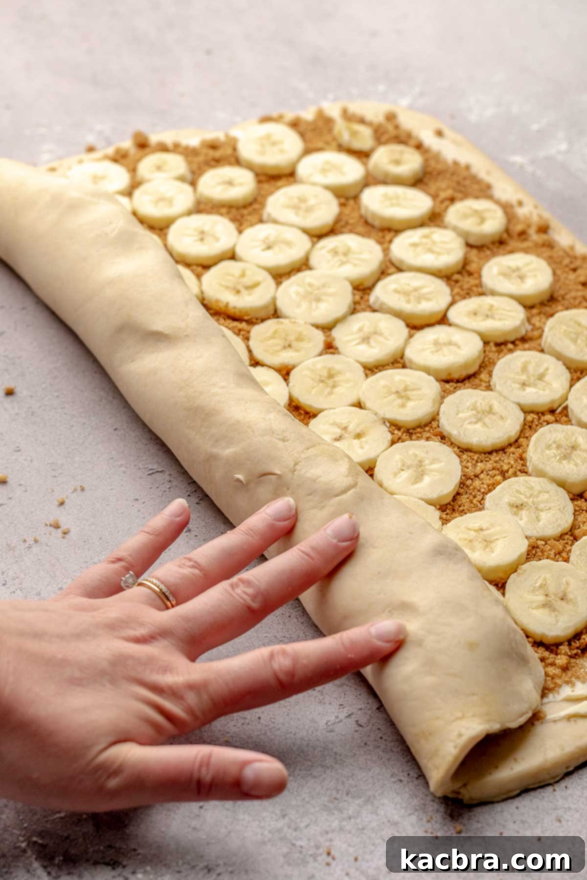 A hand meticulously rolls up a log of banana cinnamon rolls, ensuring a tight and even spiral.