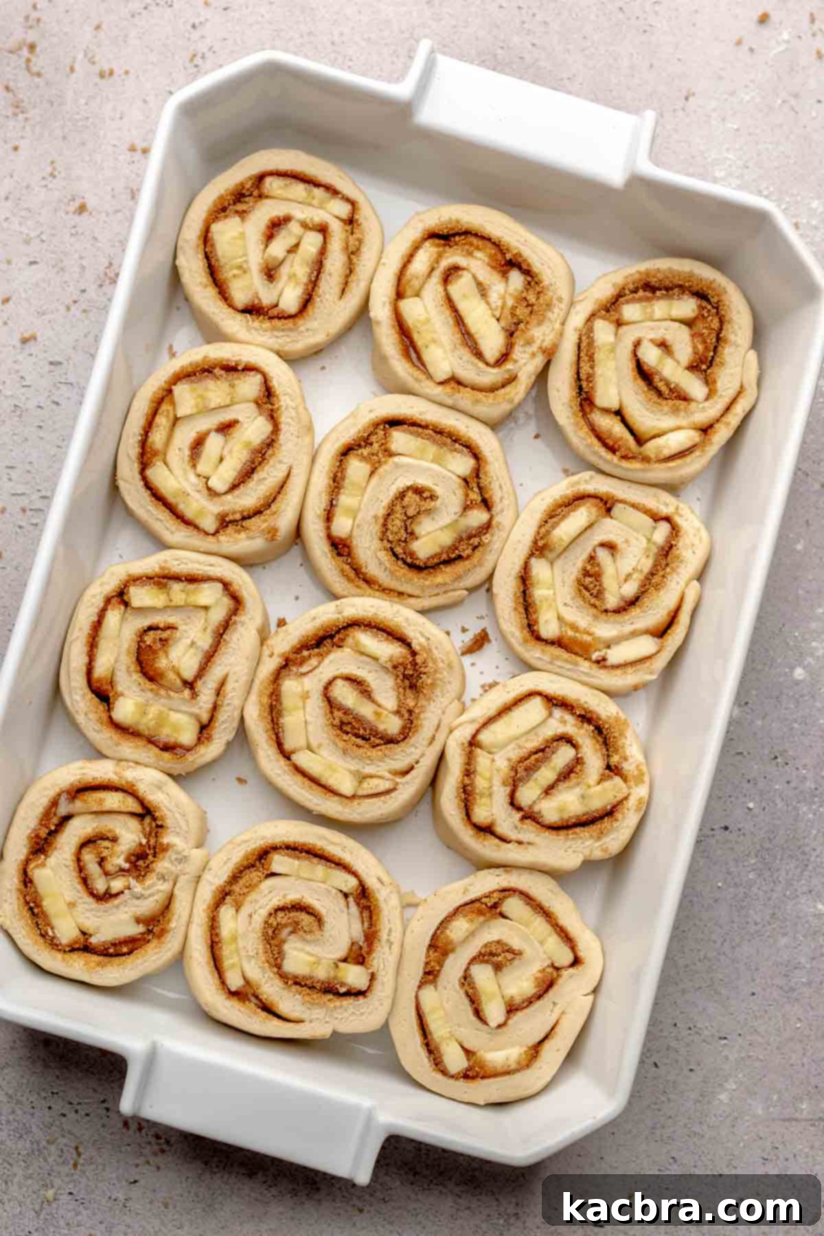 Unbaked banana cinnamon rolls neatly arranged in a 9x13 inch casserole dish, ready for their second rise.
