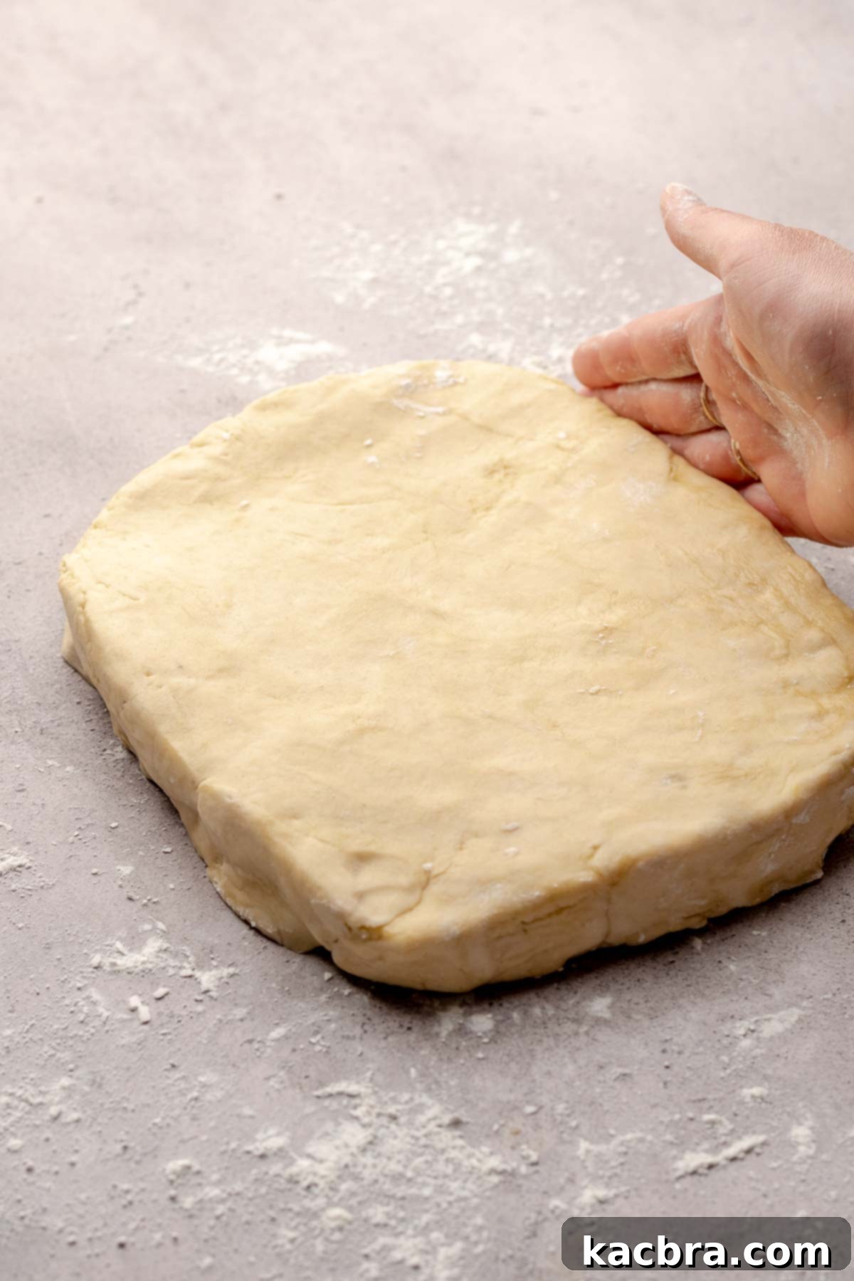 A hand gently pats cinnamon roll dough into a rectangular shape on a floured surface.