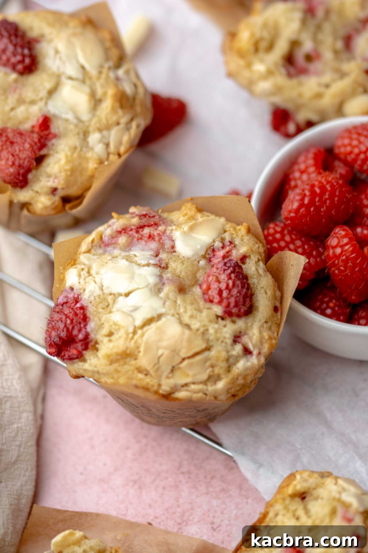 A perfectly baked raspberry white chocolate muffin next to a vibrant bowl of fresh raspberries, inviting you to indulge in its fluffy texture and rich flavor.
