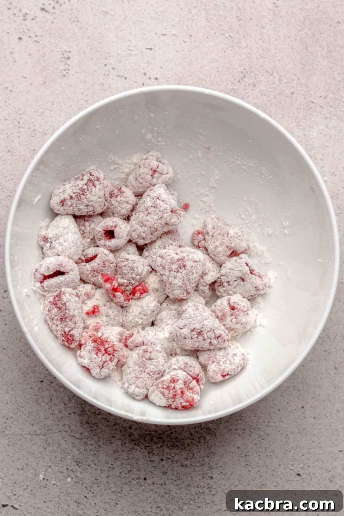 A bowl of fresh or frozen raspberries lightly coated in flour, ready to be incorporated into the muffin batter for even distribution and to prevent sinking.
