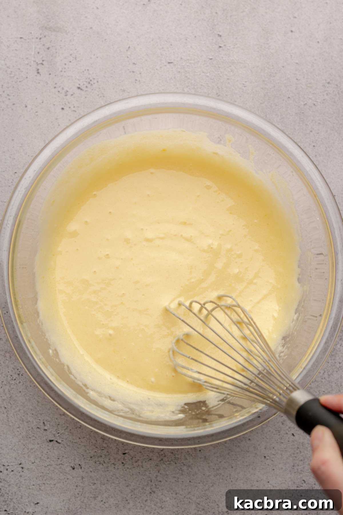 A hand expertly whisks together wet ingredients in a large mixing bowl, creating a smooth and well-combined base for the muffin batter.