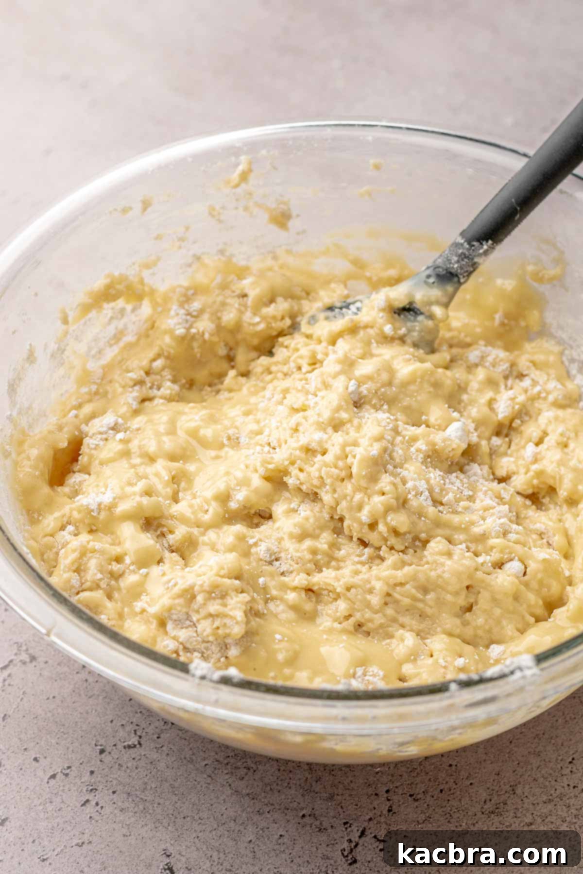 A bowl containing a lightly mixed muffin batter, with some dry flour still visible along the edges, indicating it's ready for the final additions.