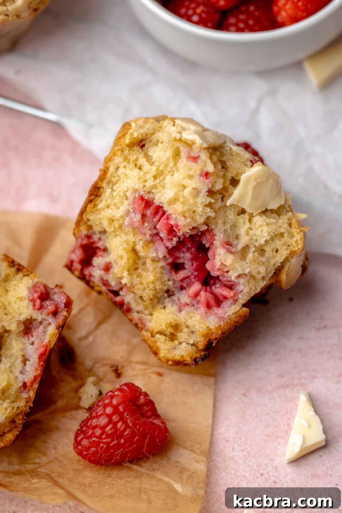 A perfectly baked raspberry white chocolate muffin broken in half to reveal its moist, fluffy interior studded with juicy raspberries and melted white chocolate.