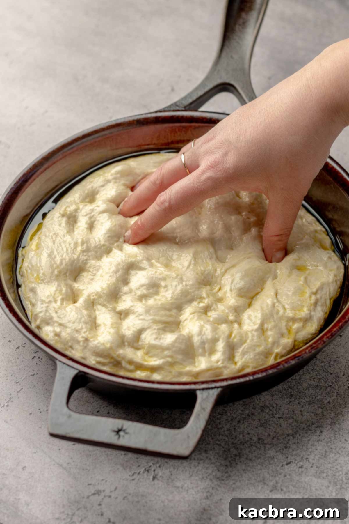 A hand spreads dough into a cast iron skillet.