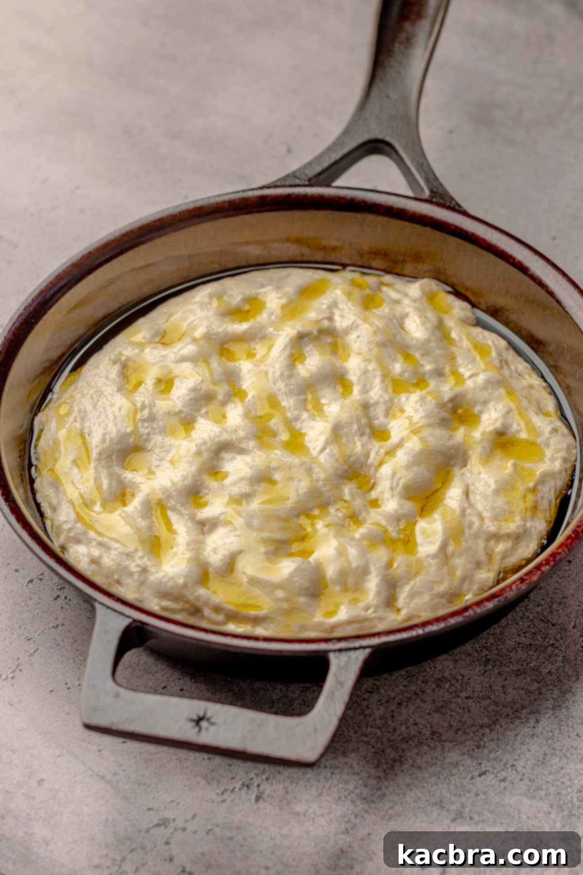 Dough in a cast iron pan with olive oil on top.