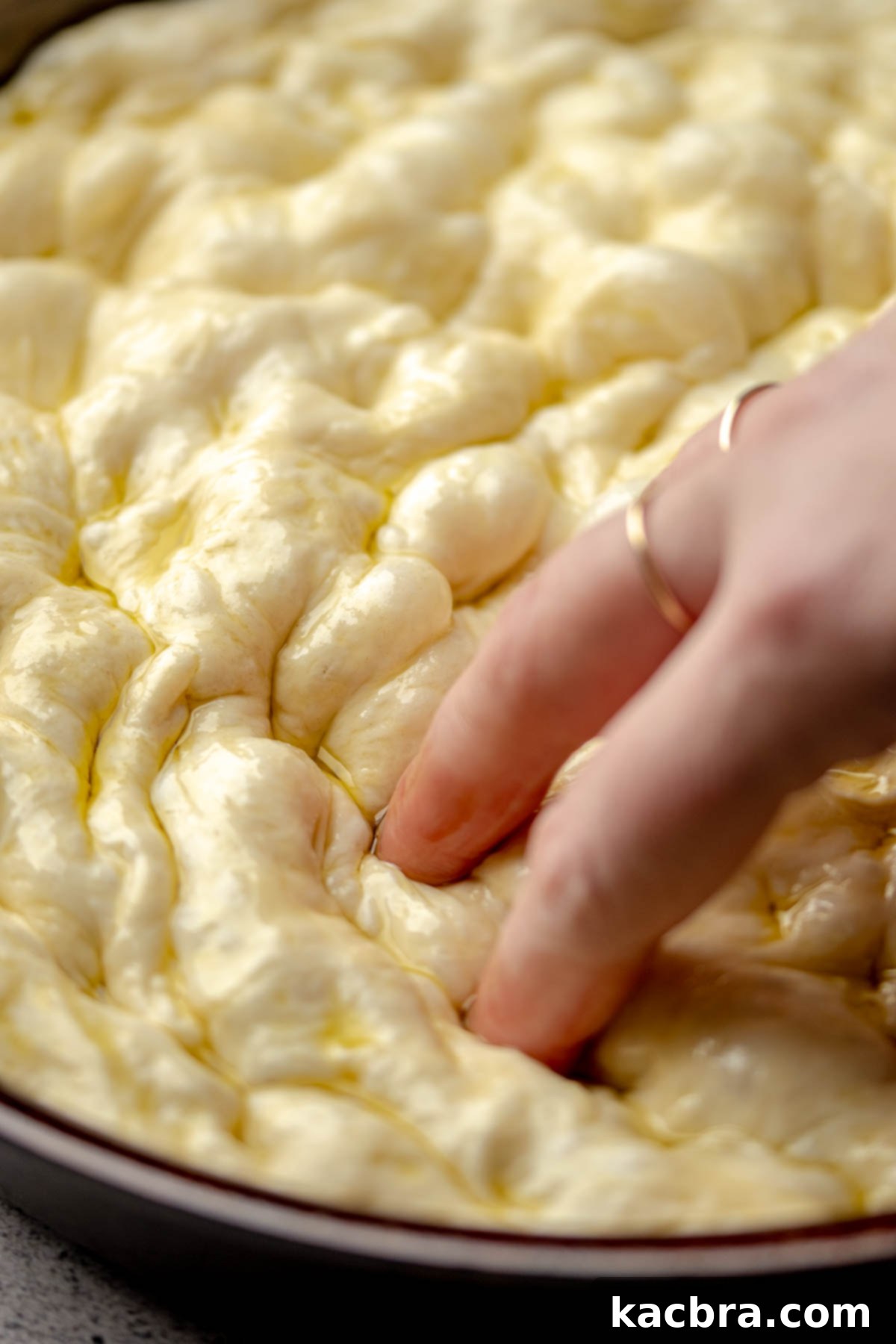 Fingers dimple pizza dough in a pan.