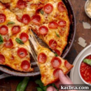 A hand pulls a piece of pizza from a cast iron skillet.