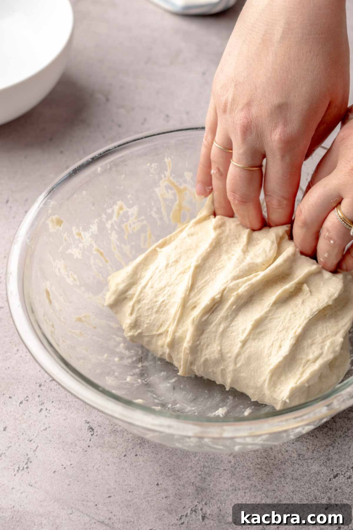 Two hands fold the dough over on top of itself in a bowl.