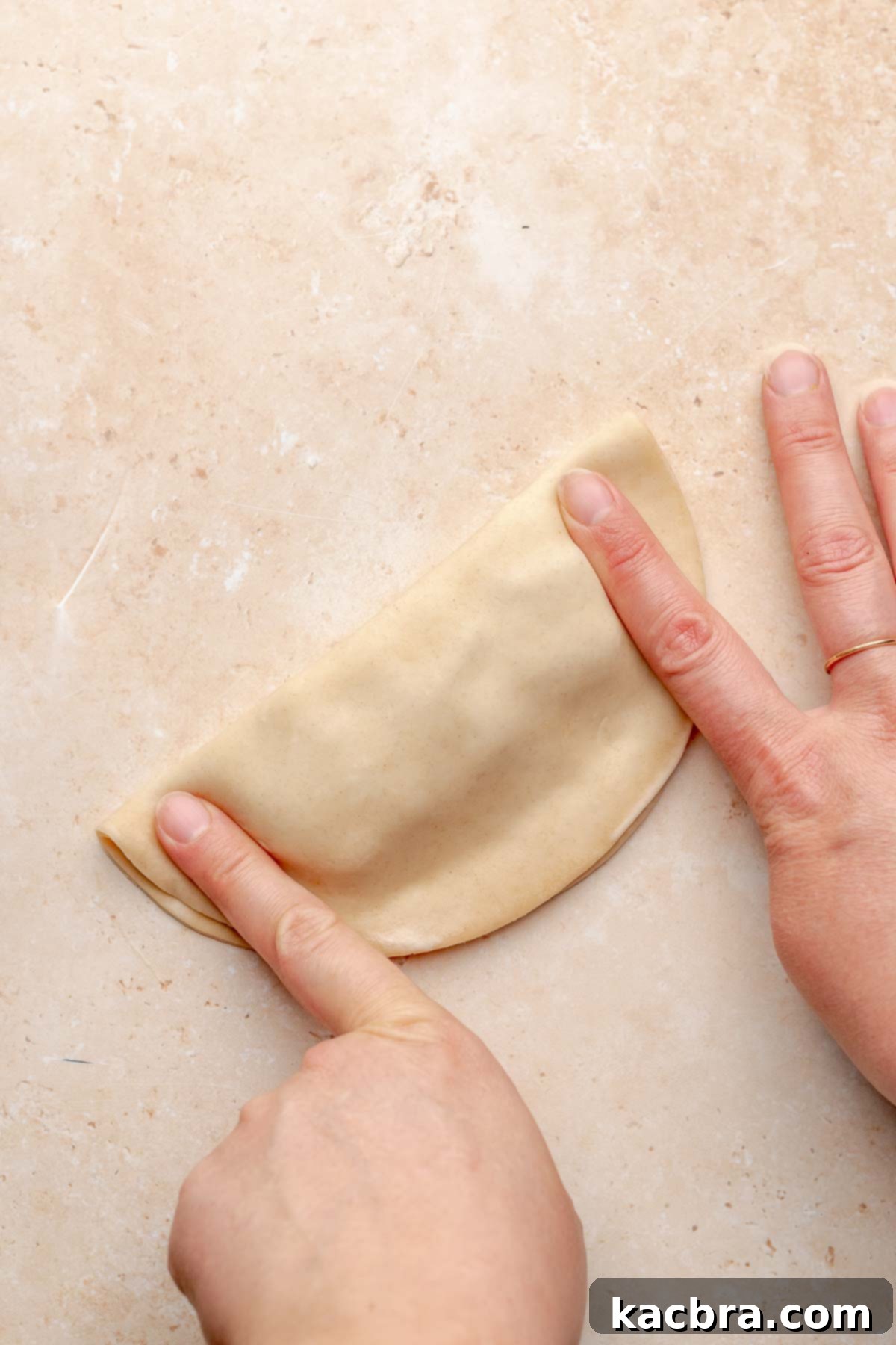 Hands press together empanada dough into a half moon.